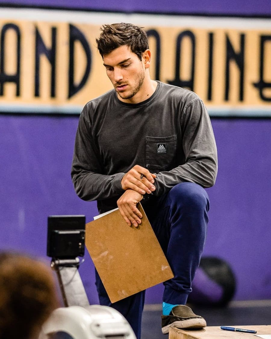 Hunter Wood coaching on the gym floor in a Misfit shirt, clipboard in hand, in front of the purple wall