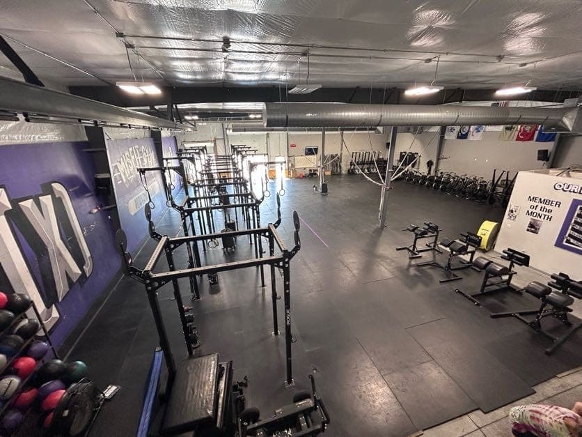 The main training floor from above: rigs and squat racks down one side under the purple Misfit mural, benches and open platform space across the rest