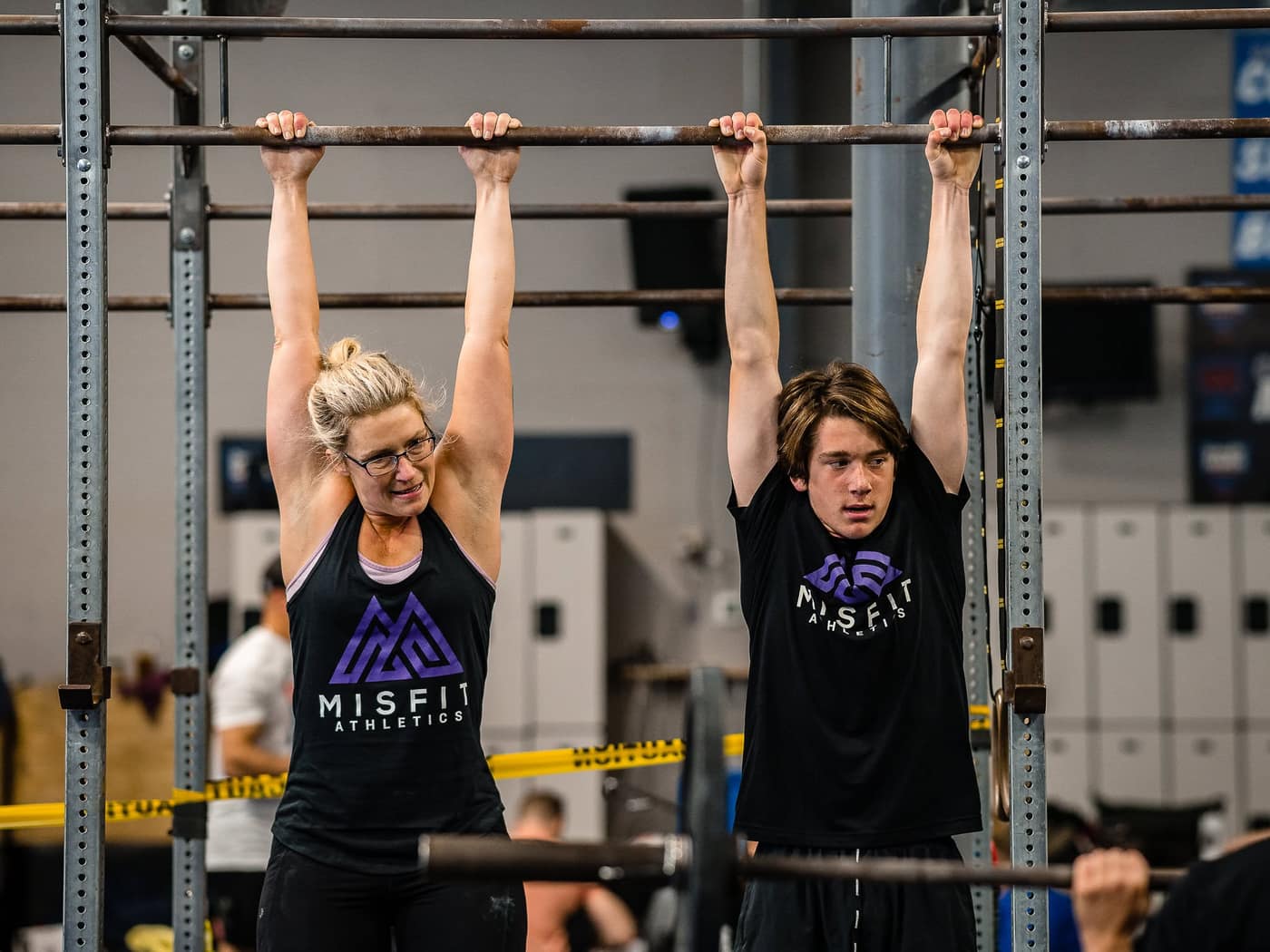 Two Misfit members in Misfit Athletics shirts hanging side by side from the pull-up rig at the start of a set