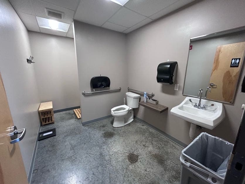 One of the restrooms: sink and mirror, grab bars either side of the toilet, paper towels, and a wooden bench