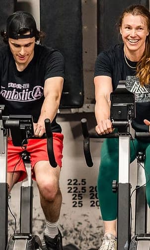 Two Misfit members riding assault bikes side by side, laughing mid-workout