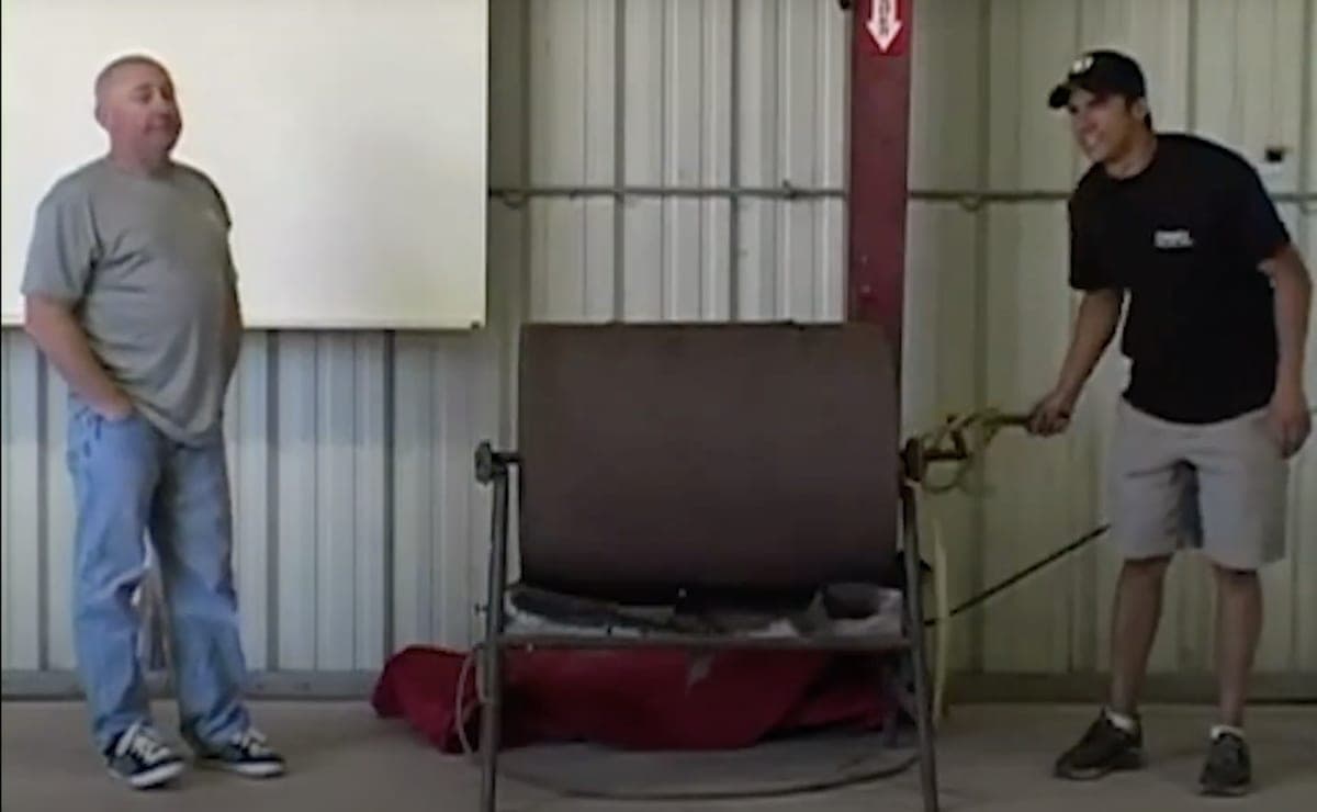 Two men either side of a rotating steel drum on a stand in a metal barn at the CrossFit ranch, the bingo-style hopper that early CrossFit Games workouts were drawn from