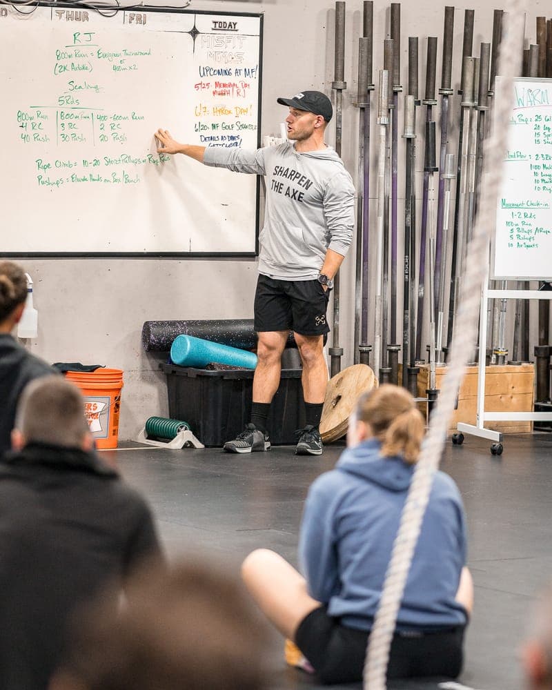 A coach teaching the day's workout at the whiteboard while the class listens